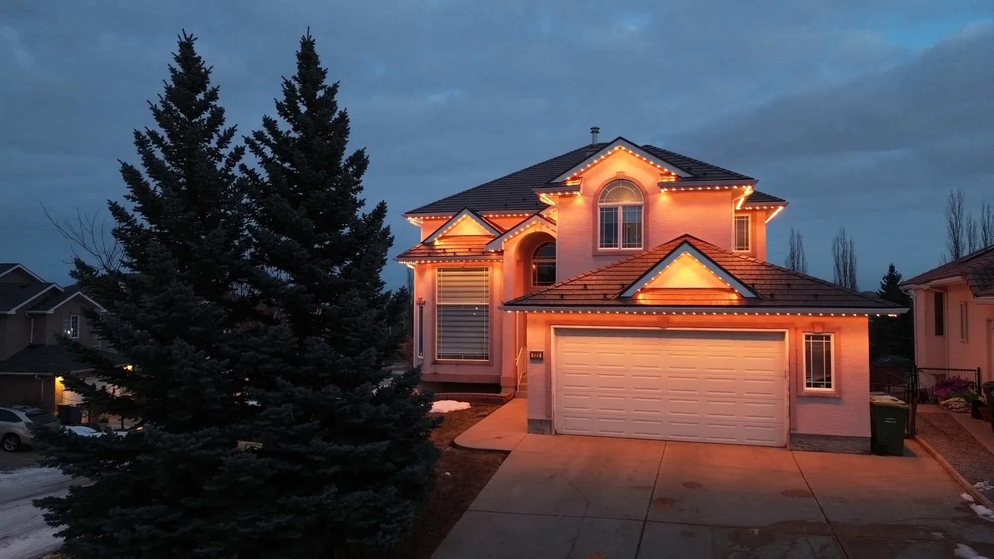Warm amber soffit lights tracing the gables and garage eaves of another two-storey home at dusk