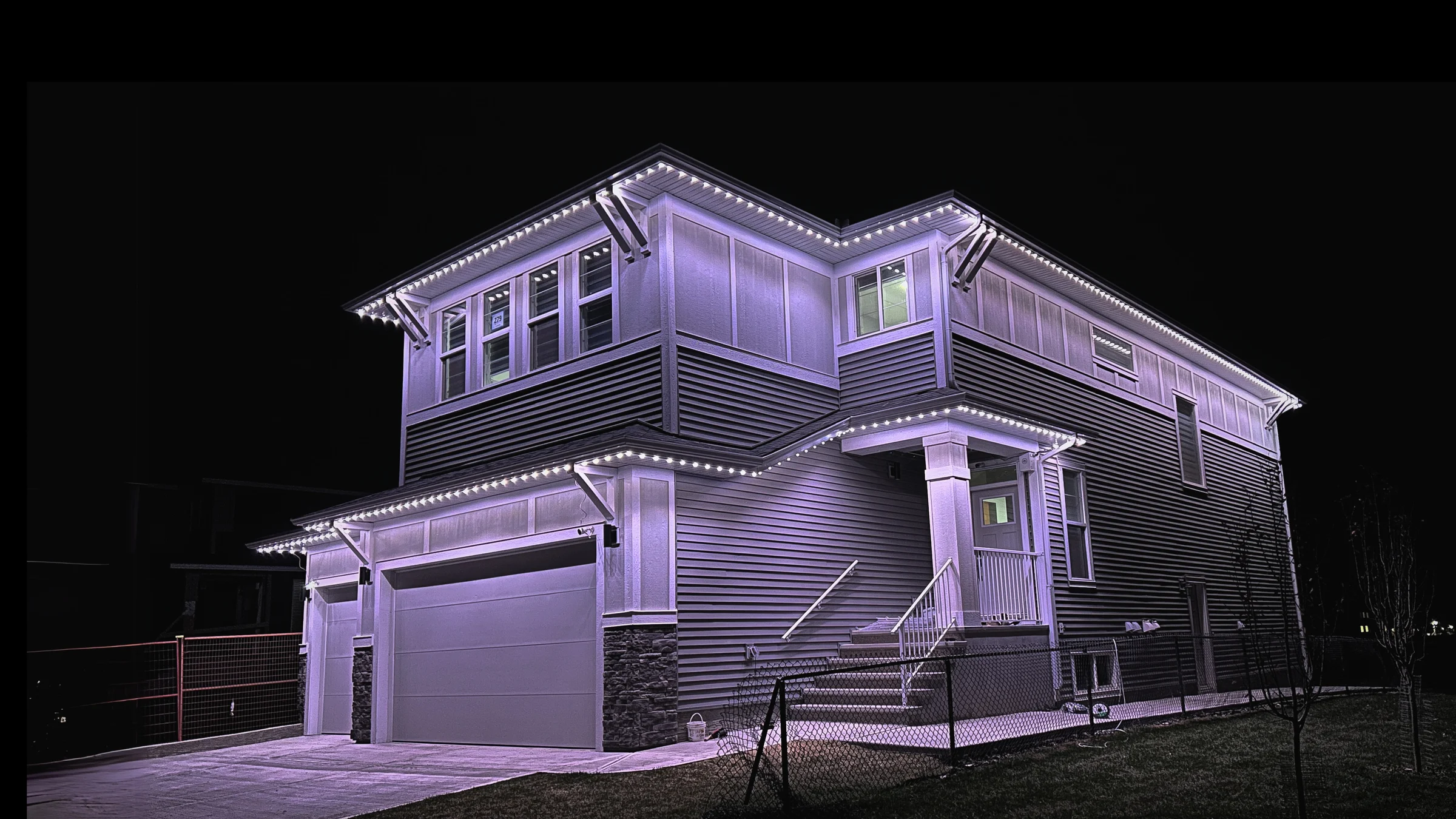 Cool-white permanent lights outlining the roofline and garage of a two-storey home at night