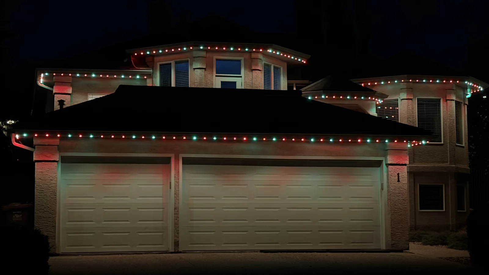 Traditional red and green permanent lights across a home’s roofline at night