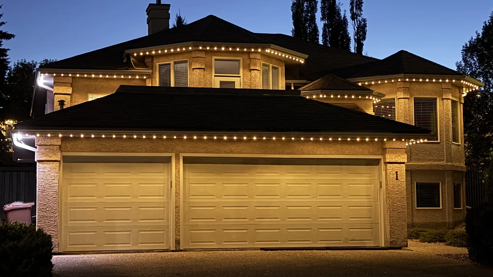 Warm-white permanent outdoor lighting illuminating the roofline of a two-storey home at dusk