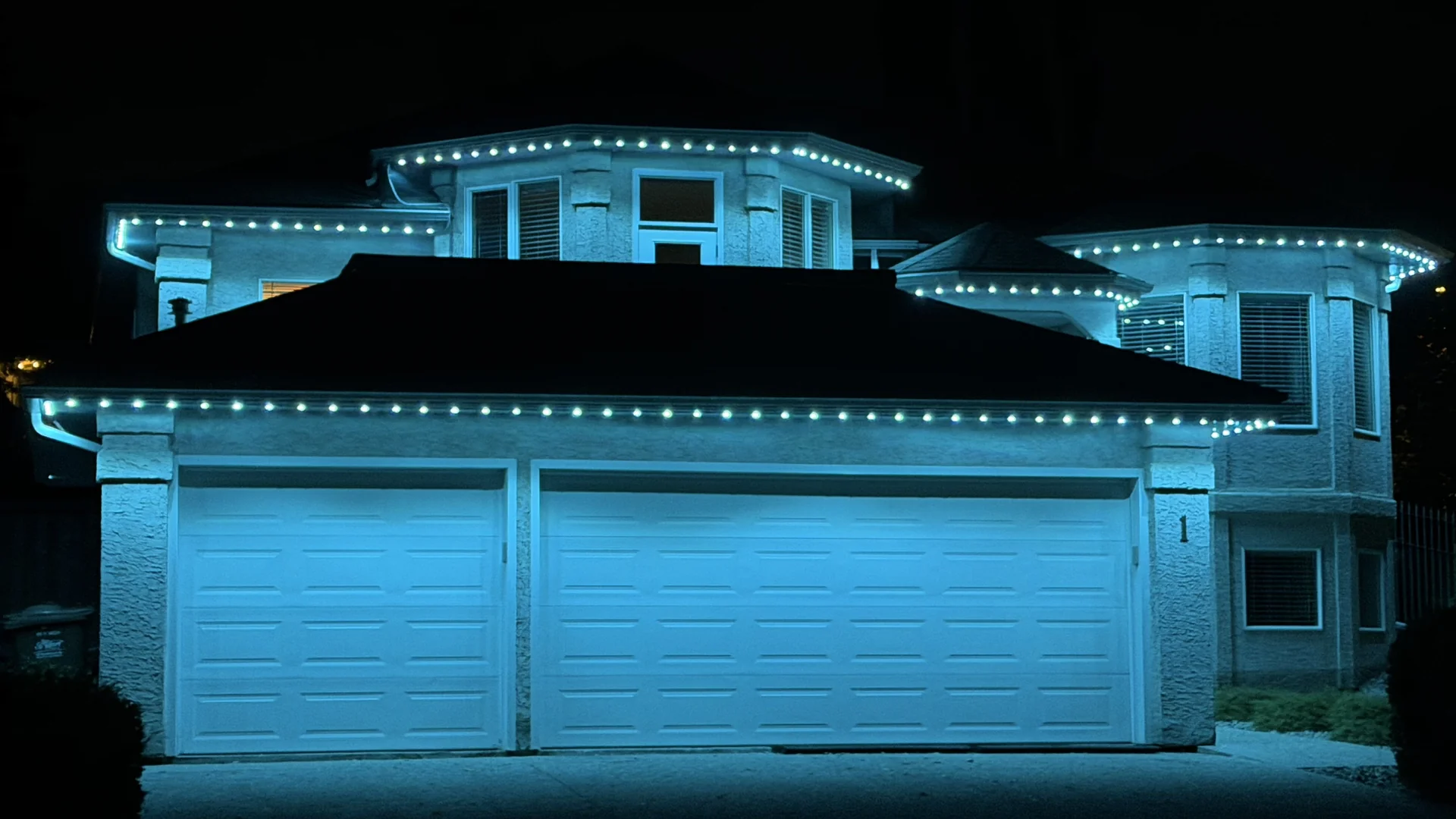 Teal permanent LED lights tracing the soffits and upper roofline of a two-storey home at night
